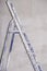 Single aluminum folding metal step ladder leaning against white plaster wall background