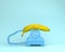 Single banana against blue retro telephone on bluish background.