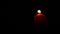 Single big red wax candle flame lights in the dark