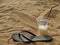 Single black beach slipper and cocktail in plastic cup with drinking straw on beach in holidays