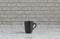 Single black color coffee mug on a front view kitchen counter top with gray tiled brick wall, 3d Rendering, close-up view