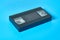 Single black old plastic vhs video cassette lies on blue desk. Concept of 90s