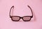 single black plastic 3d glasses on coral pink background, temple arm of eyeglasses are open, closeup