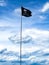 A single black skull and crossbones pirate flag waving in the air against a blue sky and clouds