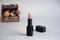 Single black tube of natural color lipstick on blurred gray background with box filled natural chestnut fruit and sycamore seeds.