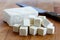 Single block of white tofu with cut tofu cubes and rustic knife