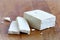 Single block of white tofu and two tofu slices with crumbs on wooden chopping board.