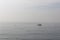 Single boat on calm ocean water on hazy morning