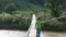 Single brave child with back passing over fragile wooden bridge, mountain river, courage