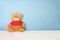 Single brown bear doll wear red shirt sit on white bed on blue background wall in bedroom look fresh like someone out it to surpri