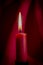 Single burning red candle against velvet drapes
