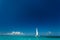 Single catamaran with tall white sail cruises in tropical waters in the British Virgin Islands