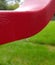 Single clear raindrop dripping off arm of backyard red chair armrest. Rainy day. Tenacity.