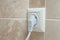 A single corner electric European wall outlet with a connected appliance with marble tiles