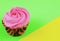 A single cupcake decorated with rose shaped pink frosting on a contrasting green and yellow background