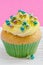 Single cupcake with yellow buttercream and colorful decorations, on pink background