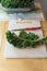 Single curly kale leaf and red handled knife on a white cutting board