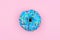 Single donut with pastel blue icing against a pink background