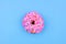 Single donut with pastel pink icing against a blue background