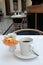 Single flower in white vase with steaming cup of coffee set on table of restaurant