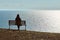 Single girl in a black jacket and hat sitting on bench at cliff at front of sea peaceful quiet place