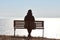 Single girl in a black jacket and hat sitting on bench at cliff at front of sea peaceful quiet place