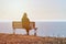 Single girl in a black jacket and hat sitting on bench at cliff at front of sea peaceful quiet place