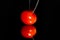 A single grape tomato on a highly reflective surface being pierced by the point of a sharp knife on a black background