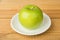 Single green apple in white saucer on table