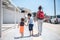 Single mother with two children walking at sidewalk summer vacation resort on warm sunny hot day holding hands shoot from back