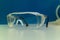 Single pair of clear protection goggles on a table inside a science laboratory isolated against blue background shallow depth of