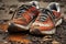 A single pair of shoes, covered in thick mud, are seen resting on the ground, Close up of well-worn running shoes after a long run