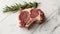 Single raw lamb chop with a sprig of rosemary on a marble countertop.