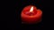 Single red heart-shaped candle burning on black background, candlelight flame