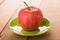 Single red striped apple in saucer on wooden table