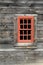 Single red window with twelve panes of glass in weathered barn wall