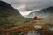 A single small red cabin billows smoke from it`s tiny chimney in the remote gorge of central Norway. The distant dark clouds give
