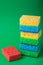 Single stack of sponges in blue, green, yellow colors near one red sponge on green paper background