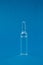 Single transparent glass ampoule with medicine on a blue background