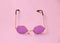 Single transparent round pink glasses on uniform coral background, temple arm of eyeglasses are open