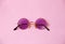 Single transparent round pink purple glasses on uniform coral background, temple arm of eyeglasses are closed, back view