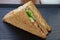 A single Tuna sandwich on black serving plate. One Club Sandwich with chicken, ham, cheese, tomatoes, cucumber, bacon, lettuce,