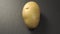 Single uncooked potato on a gray stone background.