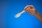 Single use disposable and biodegradable wooden spoon held in hand by Caucasian male. Close up studio shot, isolated on blue