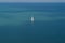 Single white-sailed sailing boat in the middle of the ocean surrounded by deep blue water.