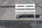 single white wooden bench is placed in afternoon sunlight on concrete floor of empty parking lot