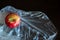 Single whole bright red yellow with small green leaf on a cellophane plastic bag. Close-up.