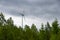 Single Wind Turbine in the middle of the green forest under blue sky with clouds. Windfarm, wind power plant