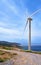 Single windmill turbine on hilltop of seashore in colorful landscape against dynamic blue sky with clouds and winding