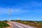 Single windmill turbine, small traditional Greek Orthodox church, road. Colorful landscape on hilltop at blue sky and